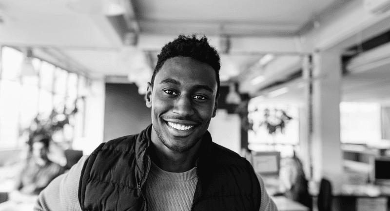 Happy young man in a puffer vest at a bright office space, showing the friendly and inclusive community spirit of our London bootcamps.