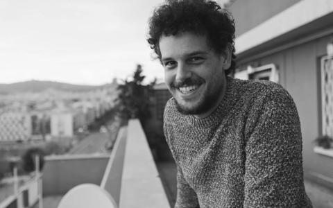 Smiling person on a balcony with a city view, enjoying a break from coding classes in Paris.