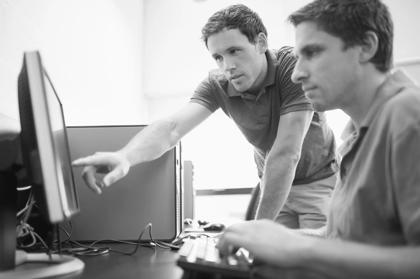 Side view of teacher showing something on screen to mature student in the computer room